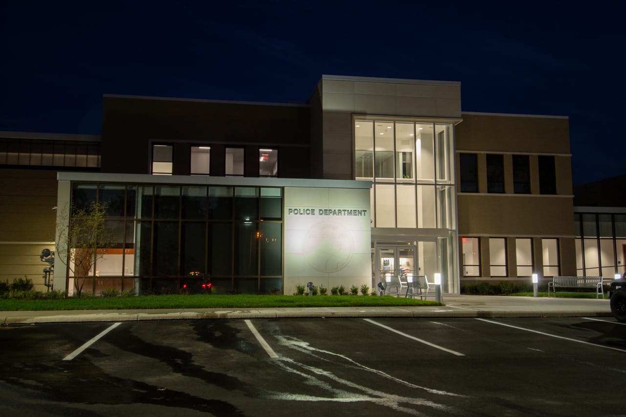Rocky River Police Station at dusk, with a lit two-story glass entrance tower and storefront wing